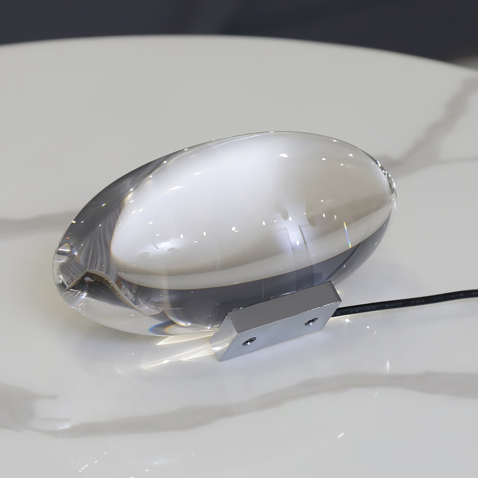 Oval dekorativ bordlampe med transparent linseformet krop og indvendig glød