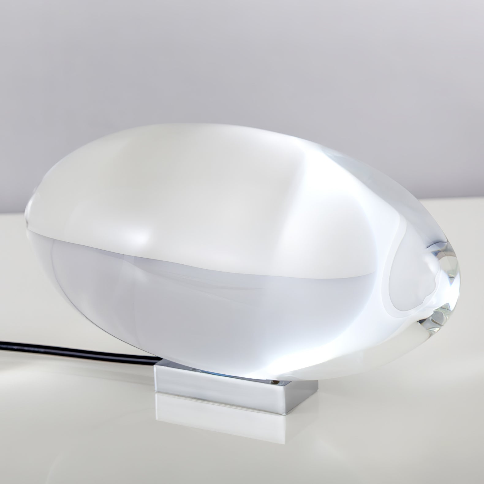 Oval dekorativ bordlampe med transparent linseformet krop og indvendig glød