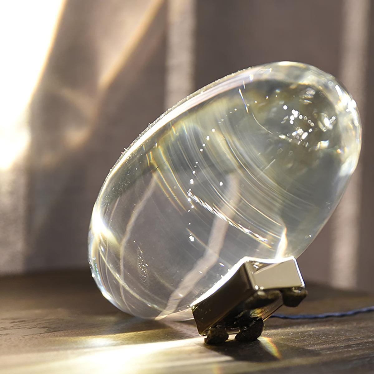 Oval dekorativ bordlampe med transparent linseformet krop og indvendig glød