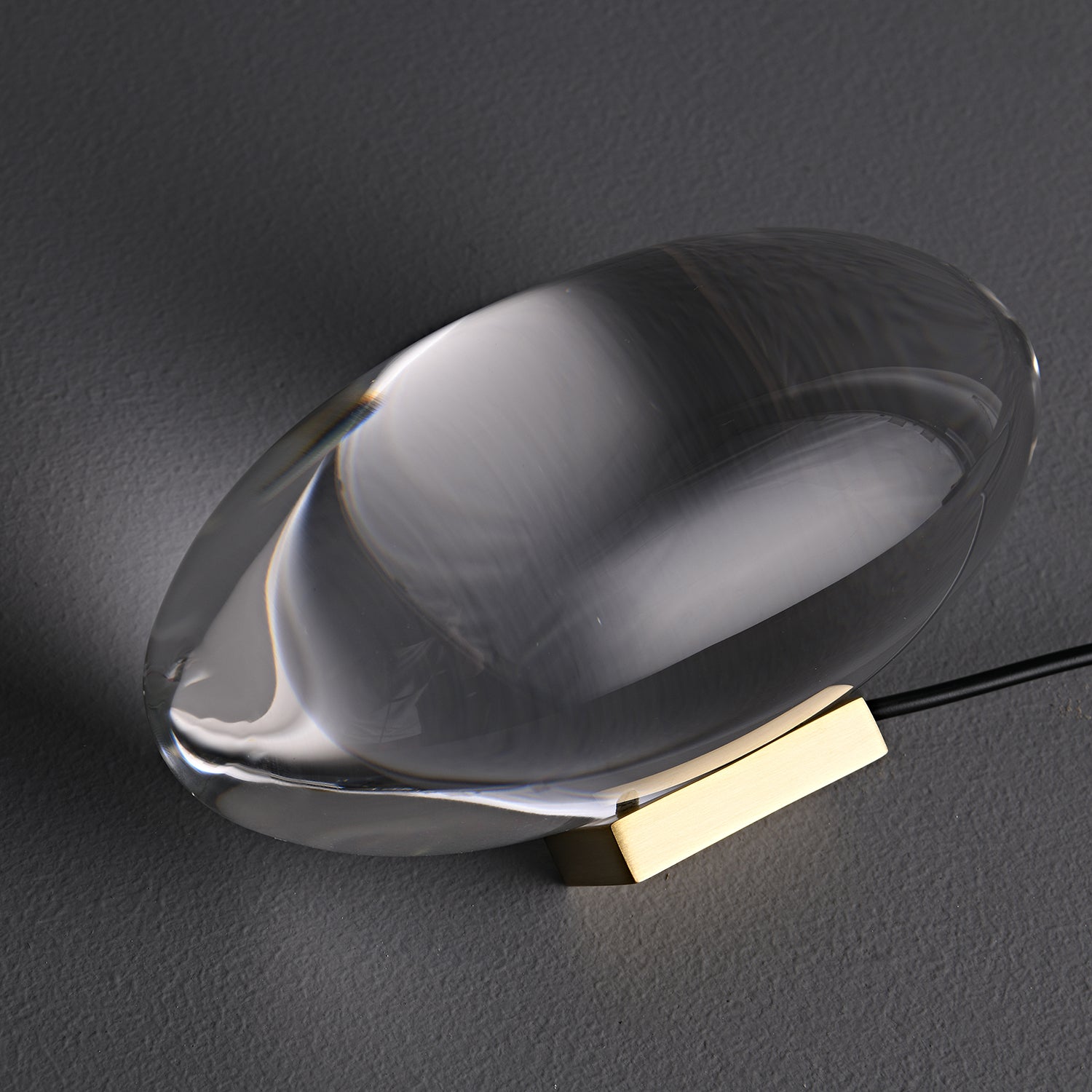 Oval dekorativ bordlampe med transparent linseformet krop og indvendig glød