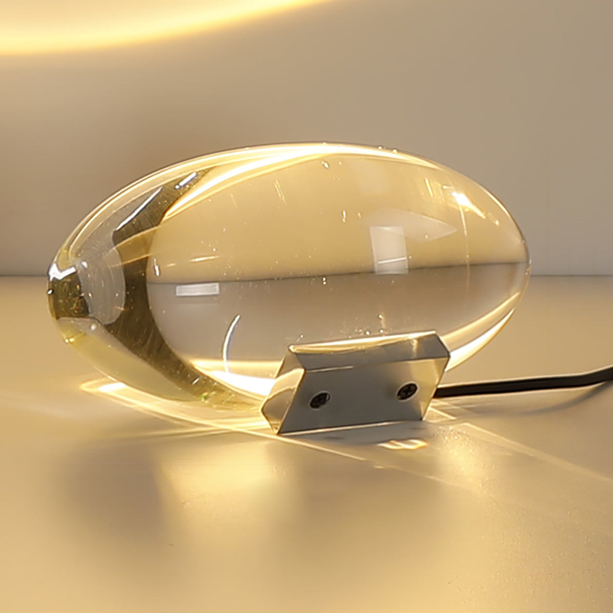 Oval dekorativ bordlampe med transparent linseformet krop og indvendig glød